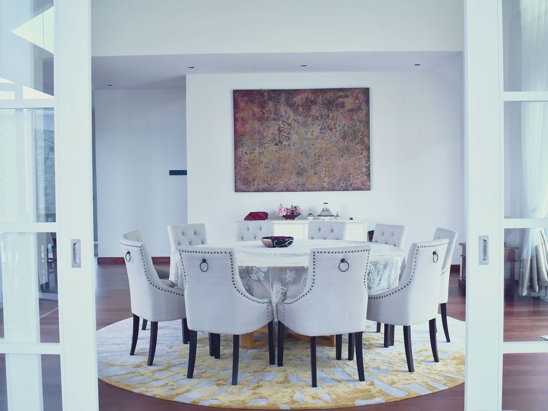 Round dining table with tufted chairs in a white double-height hall