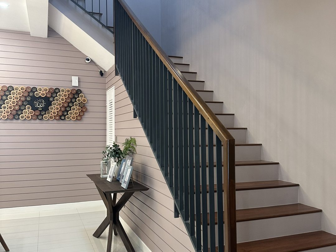 Staircase with timber treads and a black metal balustrade against a blush feature wall