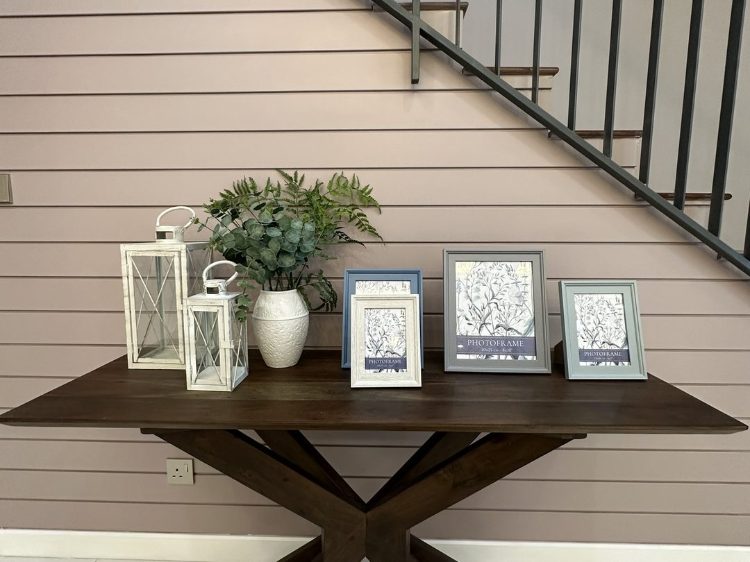 Under-stair console styled with lanterns and framed art on a blush panelled wall