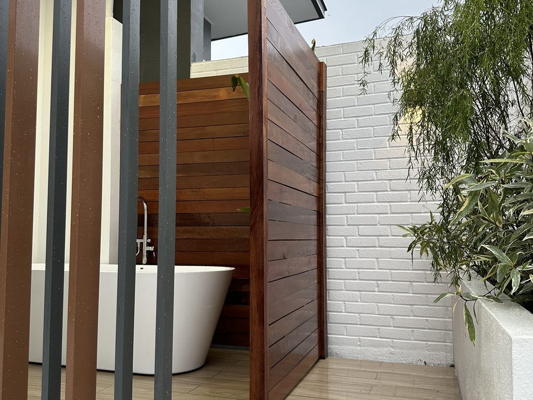 Outdoor freestanding bathtub behind a timber slat screen on a covered deck