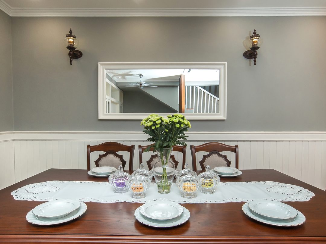Dining table set beneath a framed wall mirror